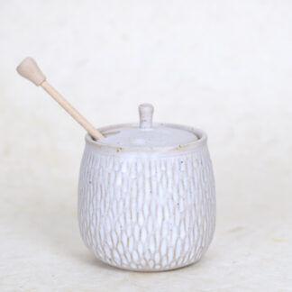 keramieken honingpot met decoratief reliëf en houten lepel