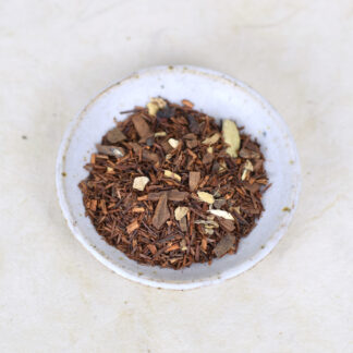 een mengeling van rooibos, gember, kaneel, kruidnagel en kardemom op een wit keramieken schaaltje