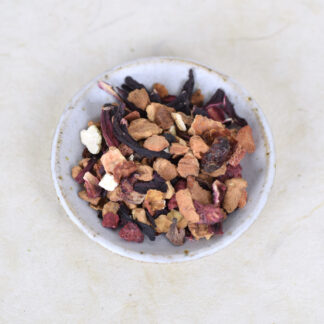edroogde stukjes appel, hibiscus, sinaasappelschil,rozenbottel, framboos, aardbei, vlierbessen en roze korenbloem op een wit keramieken schaaltje